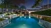 A serene poolside scene at dusk, surrounded by palm trees and illuminated by soft lights.