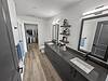 A modern bathroom featuring dual sinks, a large mirror, and a closet with hanging clothes.