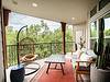 A serene balcony with a hanging chair, table, and plants, overlooking greenery.