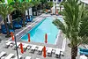 A bright outdoor pool area with palm trees and orange umbrellas.