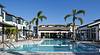 A modern apartment complex with a clear pool and palm trees under a bright blue sky.