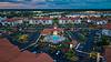 Aerial view of a residential complex with a pool and parking areas, set against a scenic landscape.