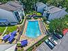 Aerial view of a swimming pool surrounded by lounge chairs and umbrellas near residential buildings.