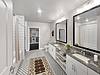 A modern bathroom featuring dual sinks, large mirrors, and a stylish rug.