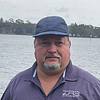 man in baseball cap and polo shirt standing near lake