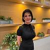 A woman in a black dress stands in front of a decorative wooden shelf with plants.