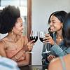 Two women clanking wine glasses and smiling.