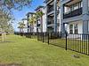Modern apartment buildings with palm trees and a fenced grassy area.