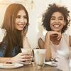Two smiling women enjoying coffee and pastries at a cozy cafÃ©.