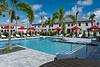 A sunny pool area surrounded by palm trees and red umbrellas.