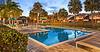 A tranquil pool area surrounded by palm trees and lounge chairs at sunset.