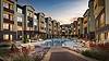 Modern apartment complex with a pool and landscaped courtyard at sunset.
