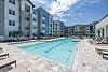 A modern apartment complex with a pool area and lounge chairs, surrounded by greenery.