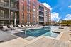 A modern apartment complex featuring a pool area with lounge chairs and clear blue skies.