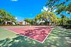 A sunny tennis court surrounded by trees and residential buildings.