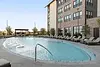 A modern pool area with lounge chairs surrounded by greenery and an apartment building.